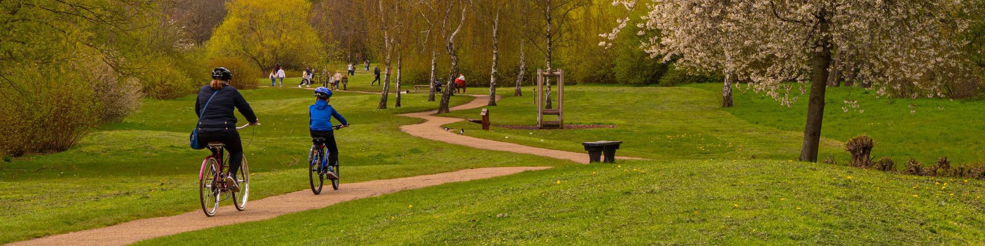 Two people cycling along pathway around Willen Lake with pedestrians in the distance