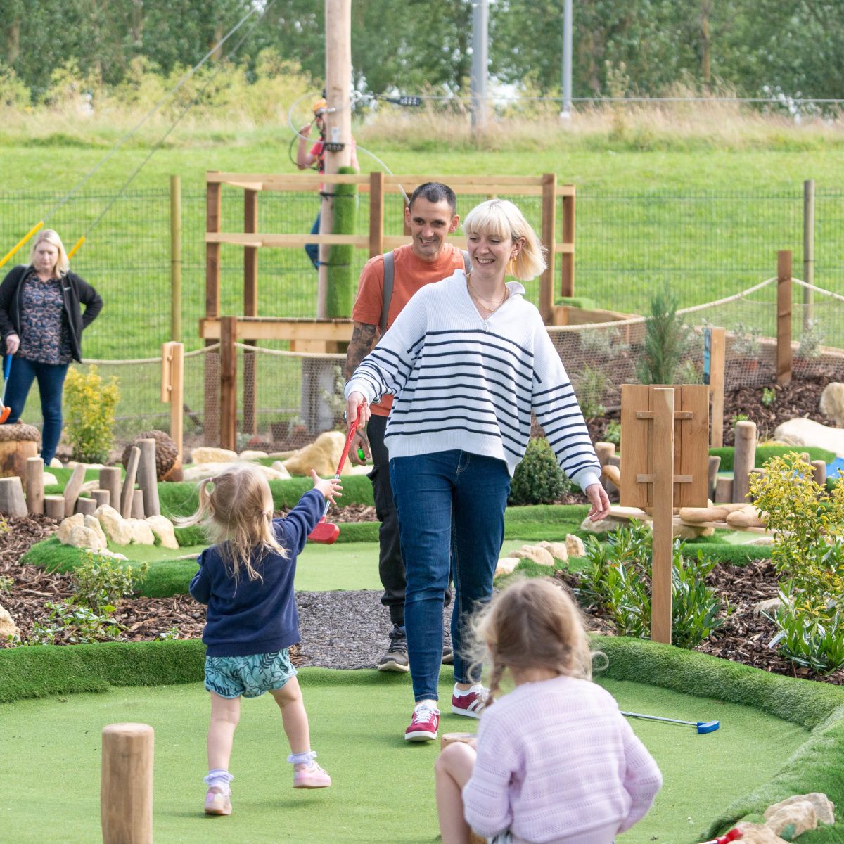 Parent passing golf club to child at Adventure Golf