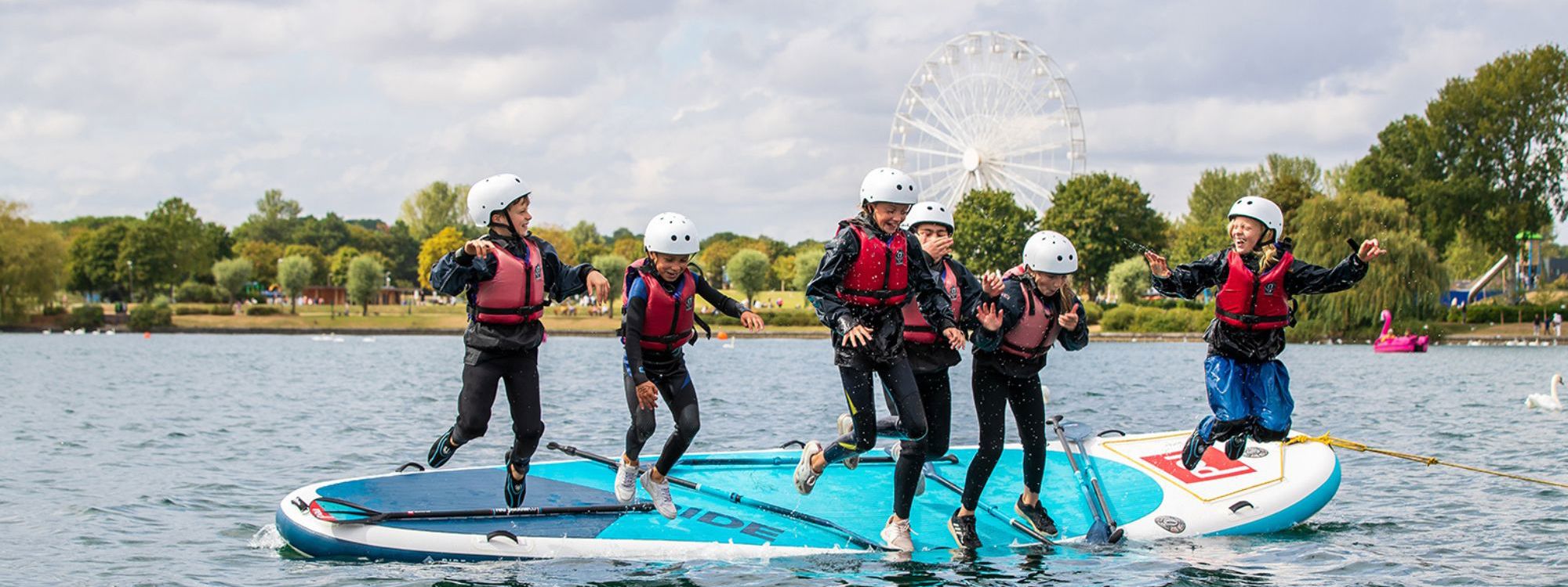 Group of children jumping off mega SUP board into Willen Lake