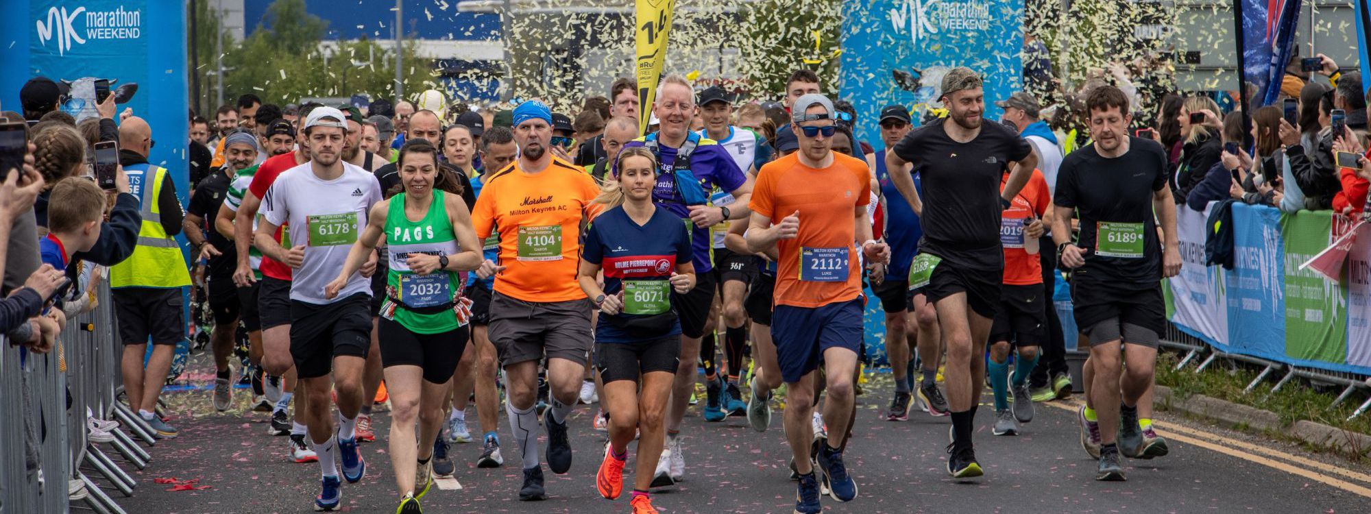 Marathon runners starting the run by passing through the blue inflatable start sign and a cloud of confetti.